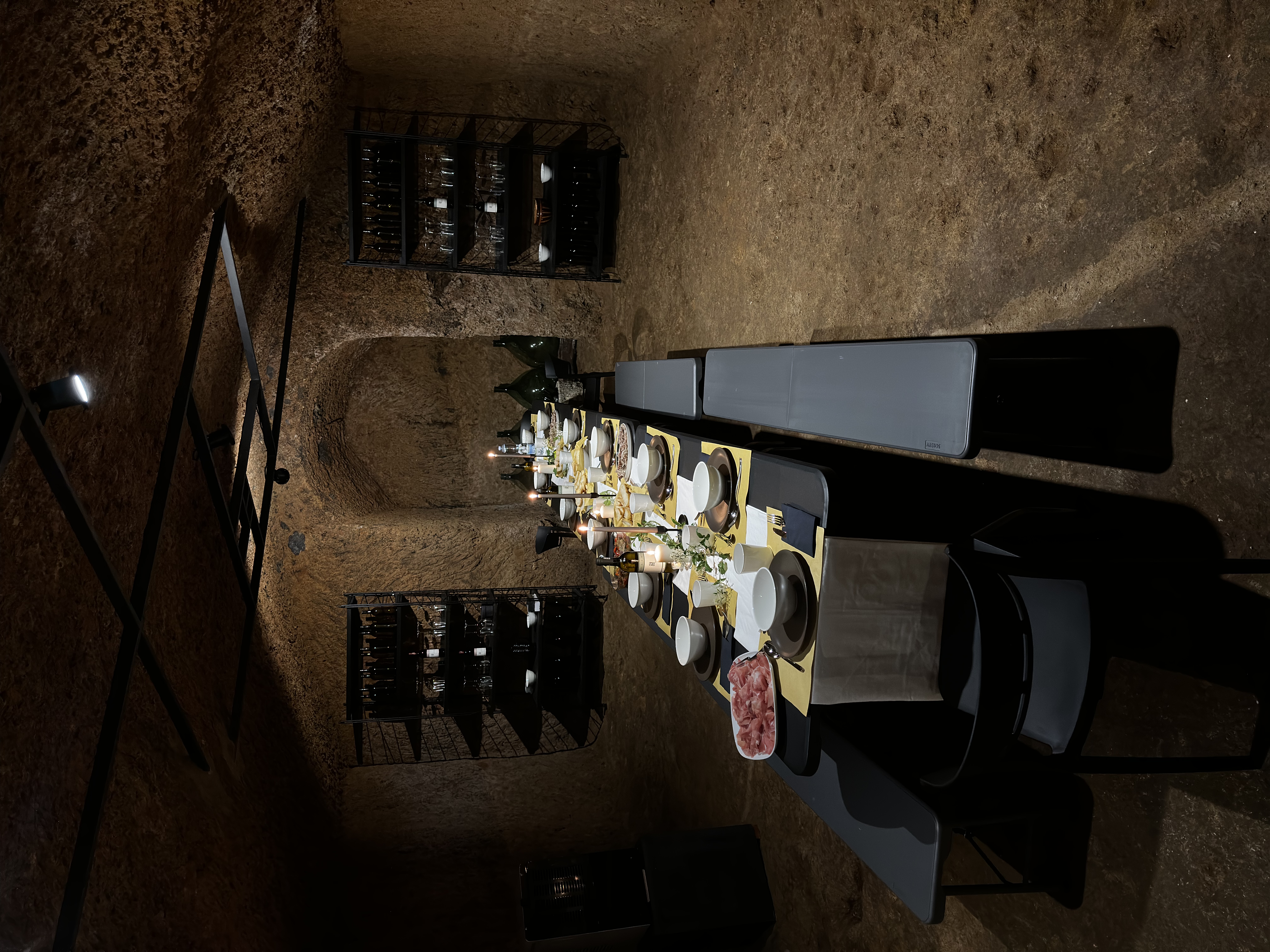 Wide view of the full cellar room with long table, twin wine racks and tuff stone walls
