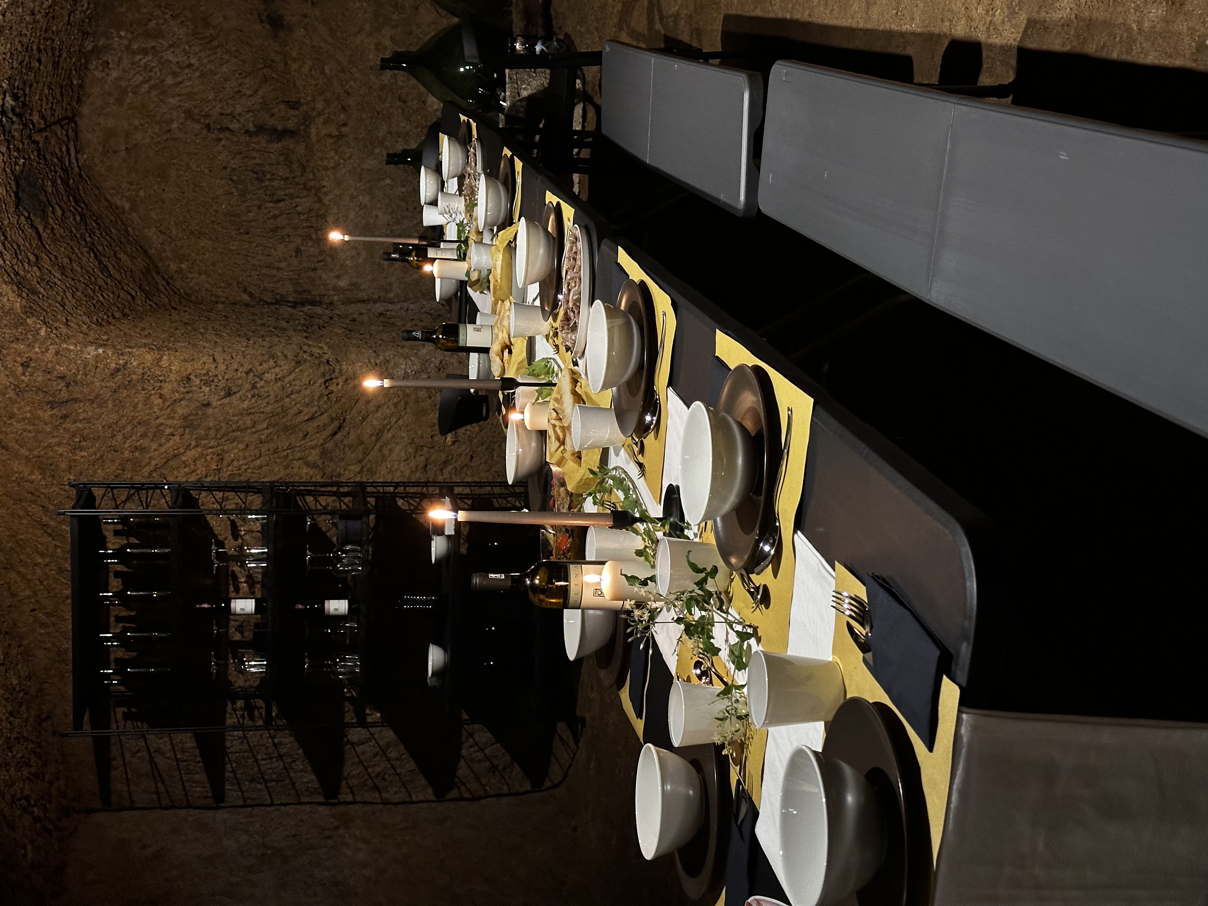 Long dining table set with food and wine, illuminated tuff stone staircase rising behind