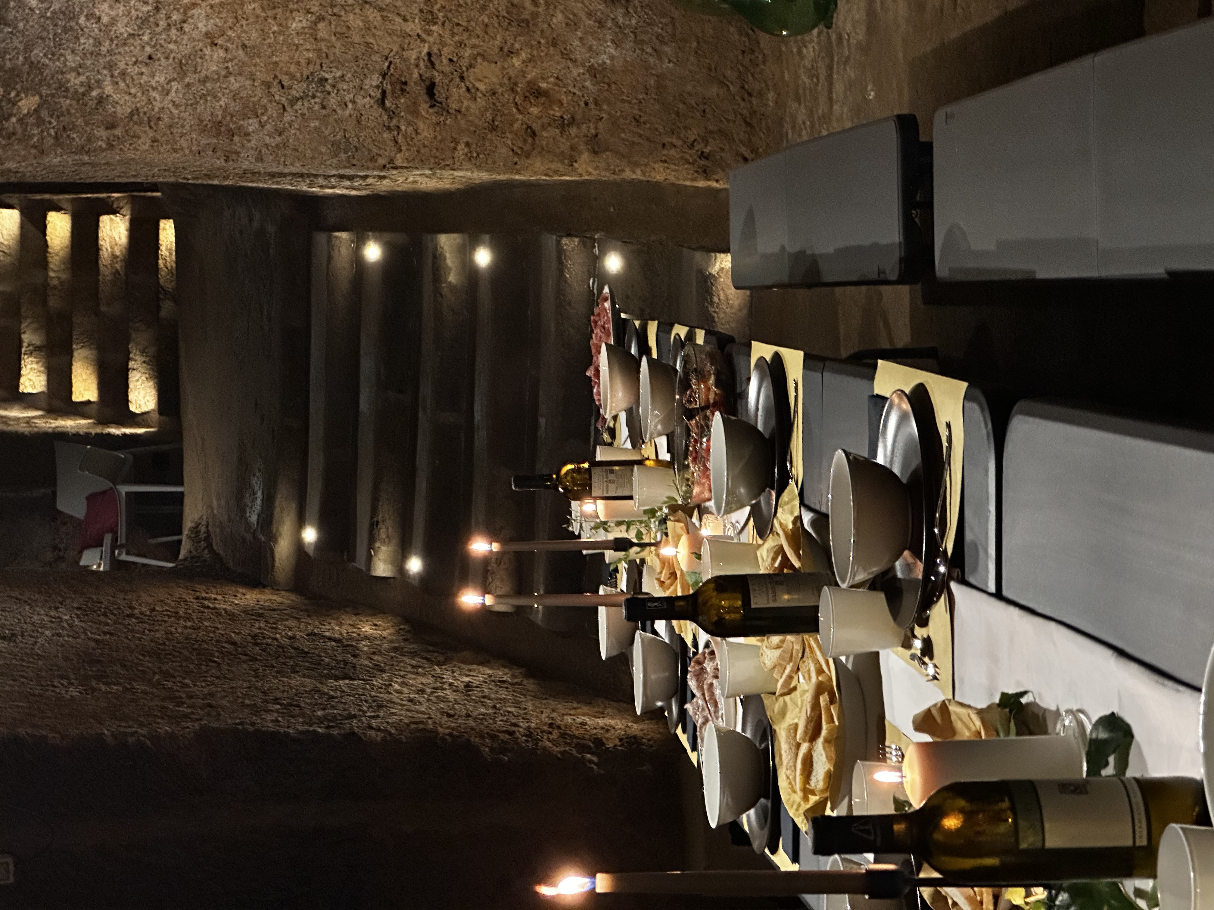 Table-level view down the set dining table, candles glowing against tuff stone walls