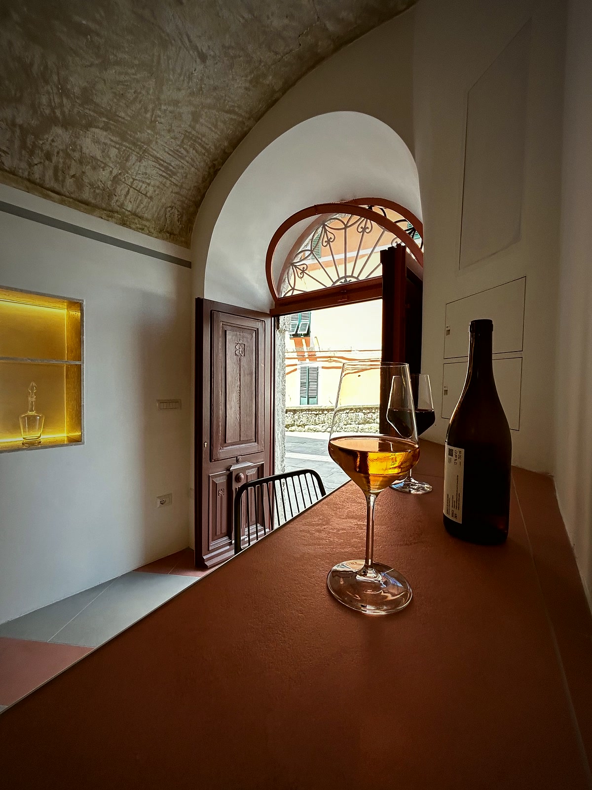Inside the Locale — the tuff-vaulted room and its long counter, an arched window open onto Piazza della Chiesa, a glass of amber wine in the light.