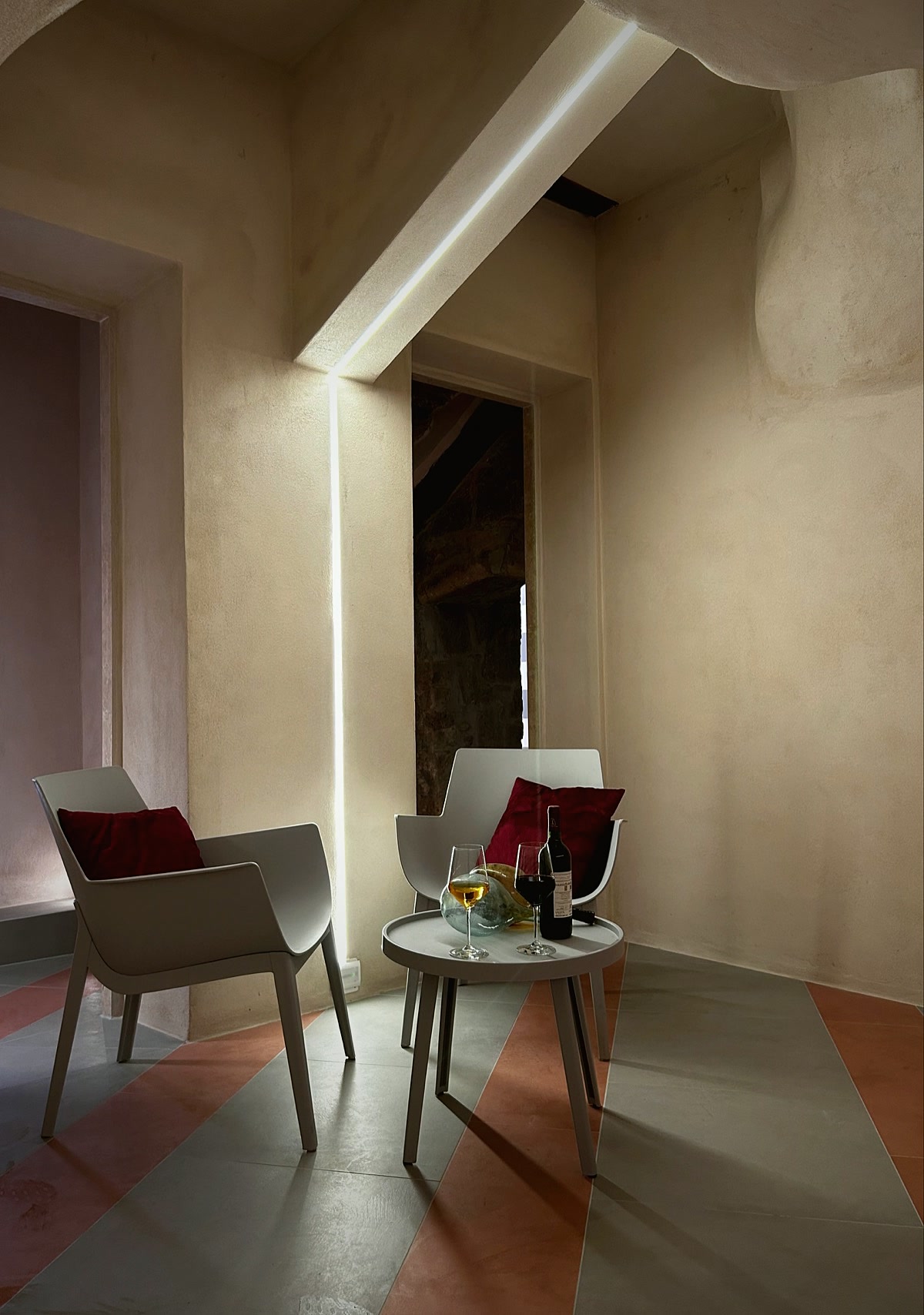 Two armchairs with burgundy cushions and a small wine table, beneath a floor-to-ceiling strip of light.