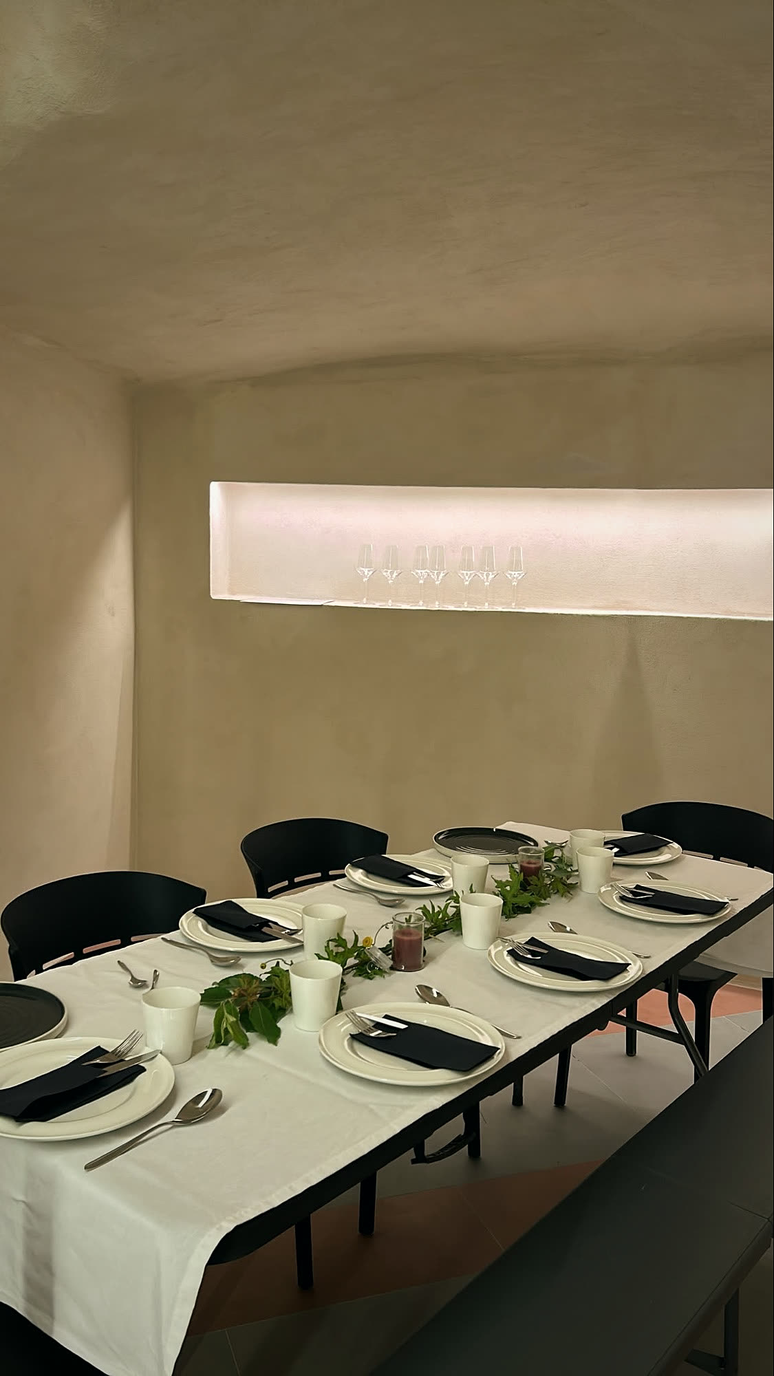 The sala — a long table set in black and white beneath a back-lit niche of glasses.