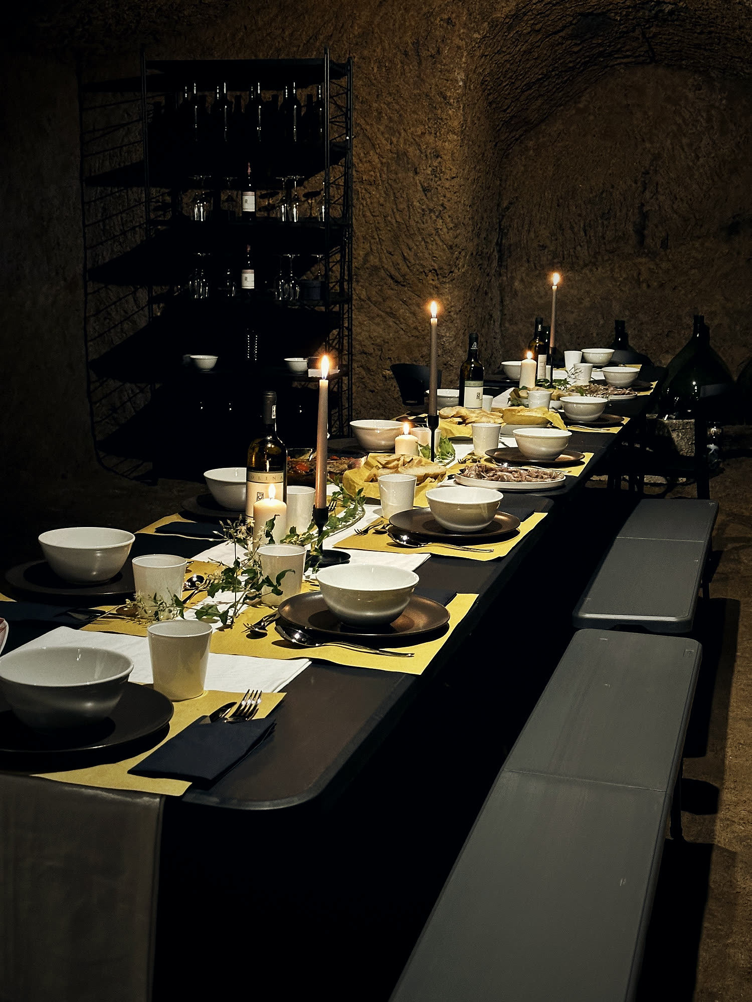 A long table laid by candlelight in the tuff cellar, the wine rack behind.
