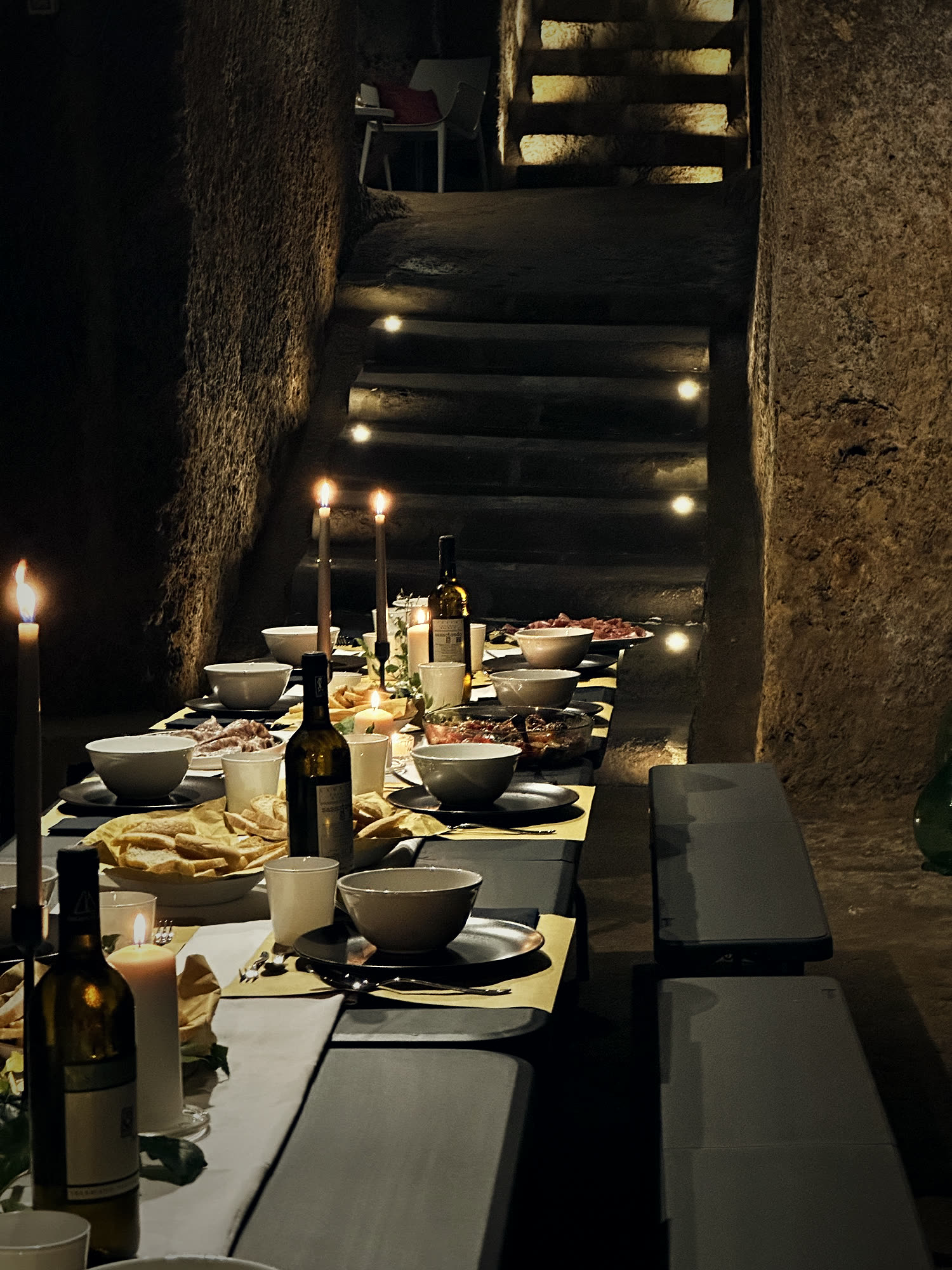 The cellar table by candlelight against the illuminated tuff wall.