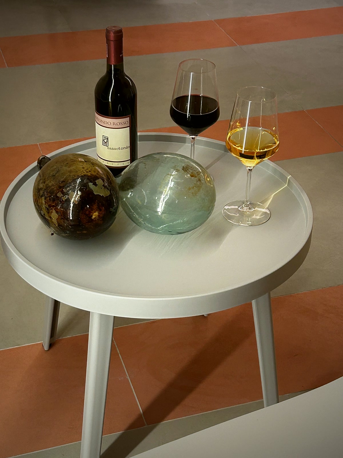 Two glasses of wine and antique glass orbs on a round table over the striped floor.